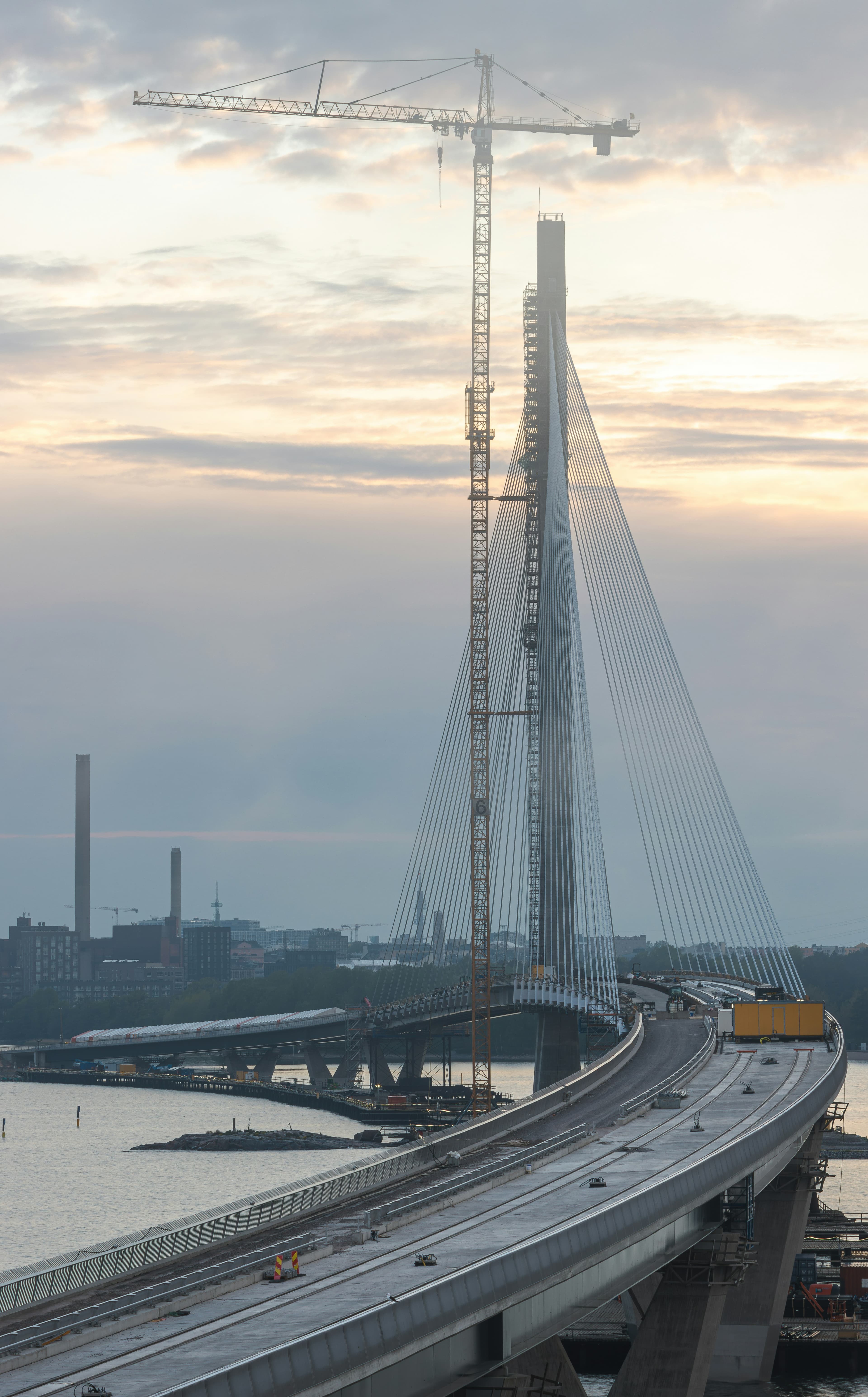 Vinoköysisilta rakenteilla merenlahden yllä, torninosturi pylonin vieressä