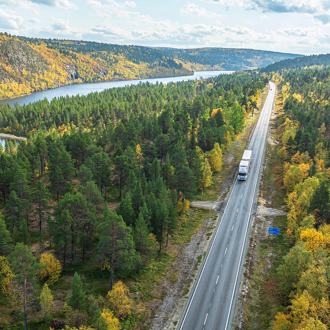 Ilmakuva rekasta maantiellä syksyisen metsän ja järven halki