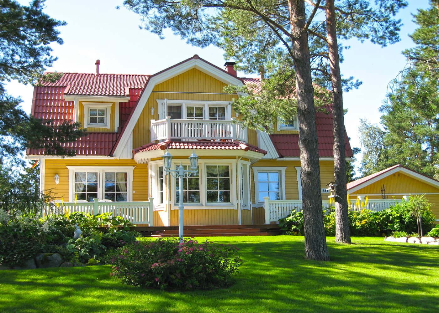 Keltainen puuhuvila punatiilikatolla ja valkoisin listoituksin kesäisessä pihassa